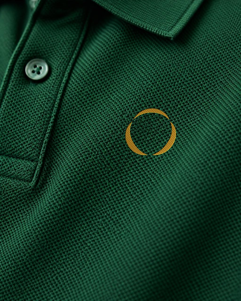 Close-up of the small amber RTP symbol embroidered on deep green piqué